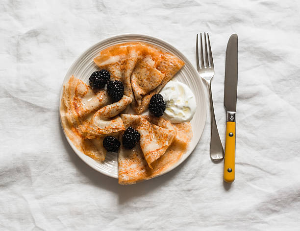 Crepes served with blackberries, yogurt and honey on a light background, top view