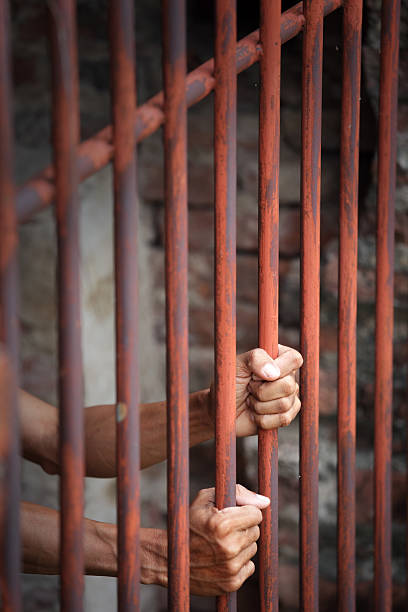 istock Hands Gripping Rusty Bars in a Dimly Lit Prison Environment 2236026038