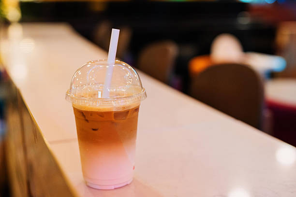 An eye-level shot of an iced latte in a clear plastic cup with a domed lid and a white straw. The drink features a striking visual gradient, with a soft pink layer at the bottom seamlessly blending into a rich brown coffee layer at the top.