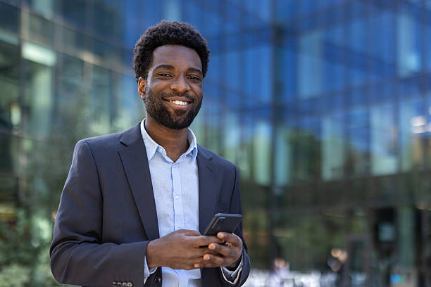 istock Smiling businessman using a smartphone outdoors near a modern glass building 2236036149