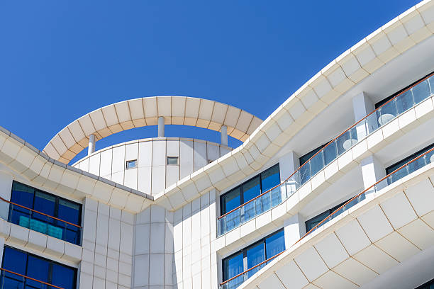 Low-angle view of a white building with blue windows and curved details against a bright blue sky.