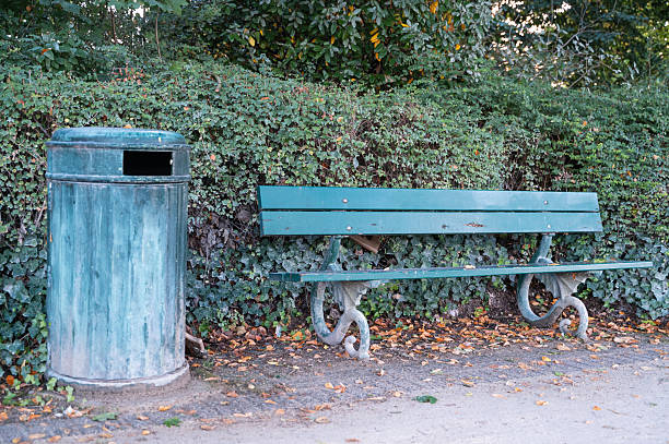 A beautifully serene park scene showcasing a lovely green bench and a trash bin surrounded by lush greenery