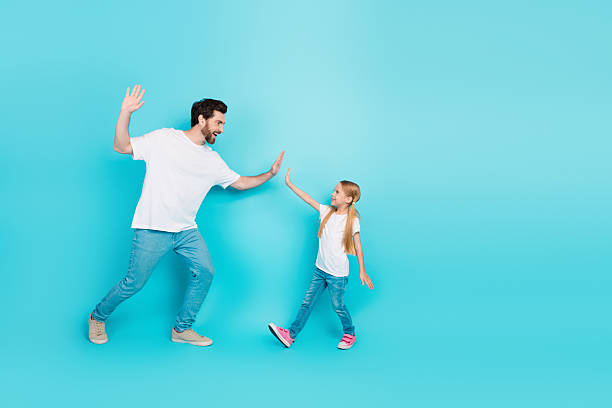 istock Young father and daughter share a cheerful high-five against bright teal background celebrating family bond and joy 2236042347