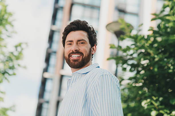 istock Confident man with a charming smile standing in an urban setting surrounded by greenery on a sunny day 2236043933