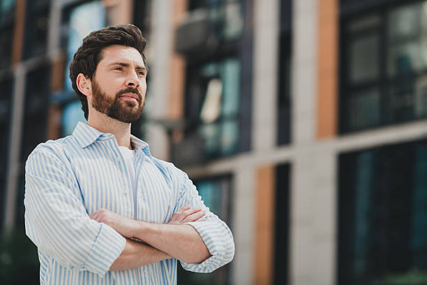 istock Confident young man standing outdoors in an urban setting with arms crossed, showcasing a modern attire and stylish look 2236044007