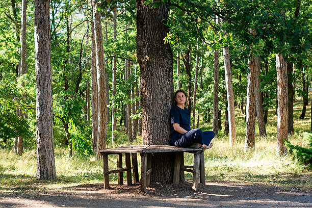 Mid adult woman enjoying the peace and quiet of nature while sitting on a wooden bench in a forest