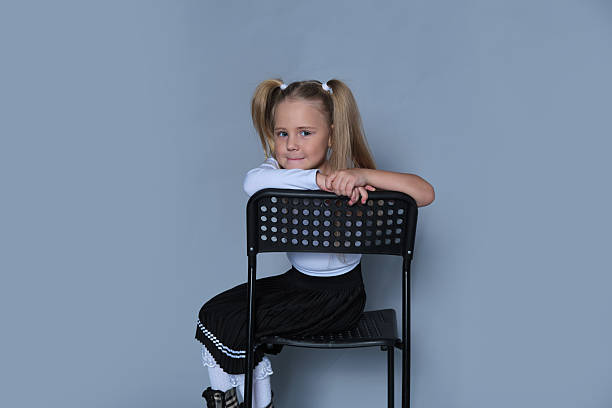 joyful 5-year-old girl laughs playfully while sitting backwards on a black chair during a studio photo session. Her lively expression and stylish outfit highlight her personality, making this photo ideal for her modeling portfolio.