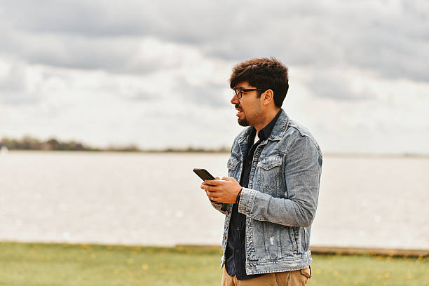 istock Young Man Outdoors Holding Phone in Casual Attire on a Cloudy Day 2236053735