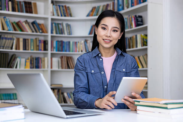 istock Smiling asian woman using a tablet and a laptop in a library. 2236059032