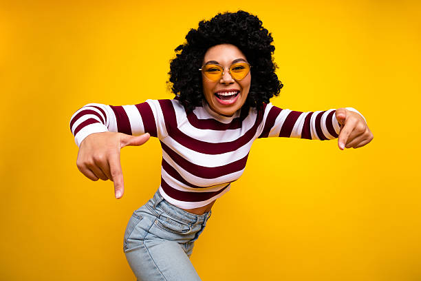 istock Cheerful young woman in stylish striped pullover gesturing confidently against vibrant yellow background 2236060099