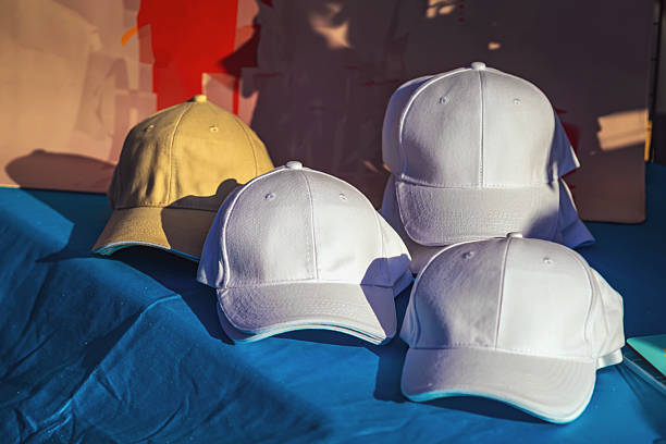 istock Plain baseball caps in white and beige are displayed on a blue surface under sunlight. Concept of fashion basics, casual style, and blank caps for customization 2236061521