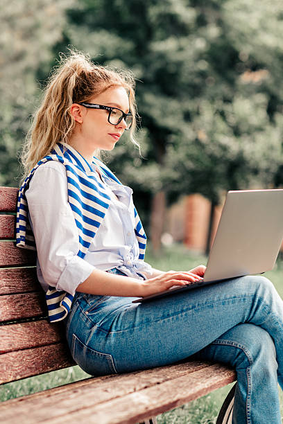 istock Young woman studying outdoors on a laptop while relaxing on a park bench during a sunny afternoon 2236061912