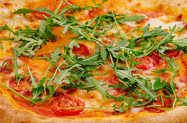 Appetizing pizza topped with tomatoes, arugula, and cheese close up background