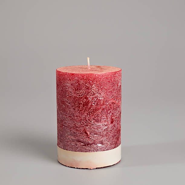 Textured deep red pillar candle with a light-colored base, featuring an unlit wick on a clean grey background. Ideal for home decor and festive themes.