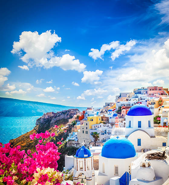 Oia, traditional greek village of Santorini with blue domes of churches under sky with flowers, Greece
