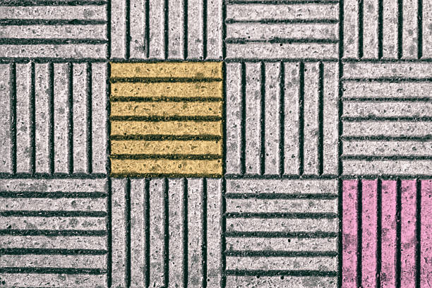 Close-up view of a pavement composed of concrete tiles featuring alternating colored squares in yellow and pink. The daylight highlights the texture and design of the surface.