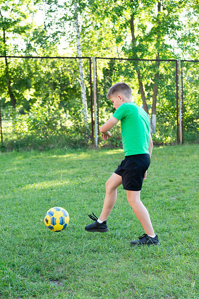 istock Boy playing soccer outdoors on a sunny day.  He kicks a ball on a grassy field. 2236078338