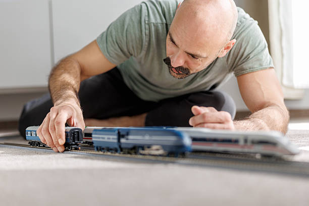 istock Middle-aged man kneeling on the floor at home and playing with model train set 2236079470
