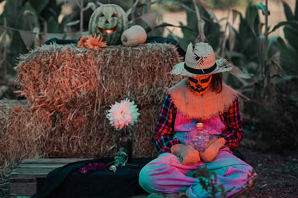 Girl dressed as a scarecrow sitting in a corn field with Halloween decorations looking down