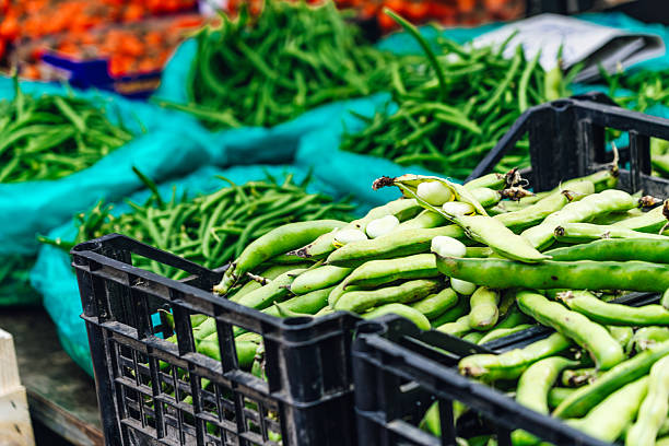 An assortment of fresh produce, including green beans, neatly arranged in crates at a Sicilian outdoor market, showcasing local culinary ingredients and the vibrant atmosphere of outdoor shopping.