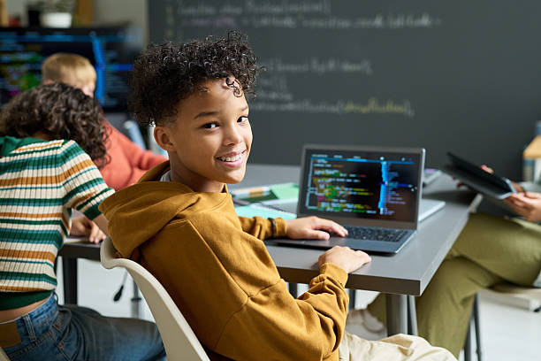 istock Portrait of Teenage Black Boy Smiling While Coding on Laptop in Classroom 2236084717