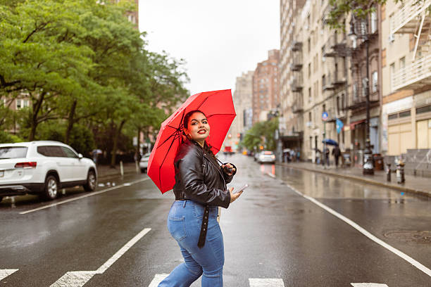 Happy woman walking across a rainy city street with a red umbrella, enjoying the weather
