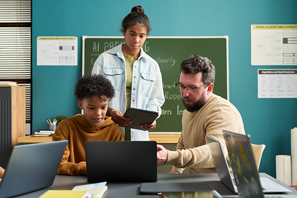 istock Caucasian Man Teaching Two Black Teenagers Using Laptops in Classroom 2236086424