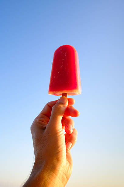 Hand holding melting strawberry ice cream against blue sky