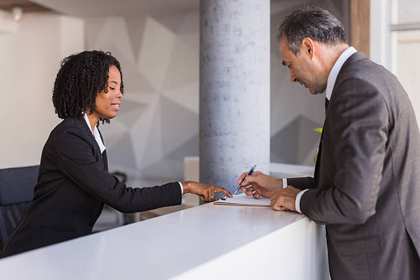 istock Businessman signing documents at reception desk with receptionist assisting 2236090114