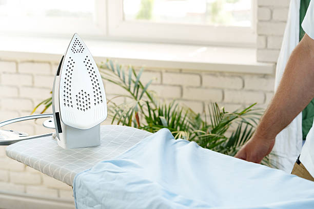 Ironing a light blue shirt on an ironing board with a sunny window background