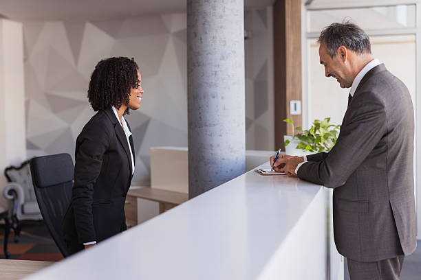 istock Businessman filling form at reception desk with receptionist assisting 2236090337