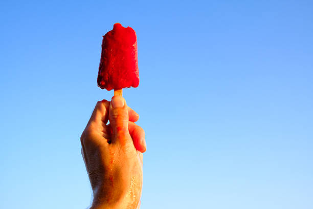 istock Hand holding melting strawberry popsicle against blue sky on summer day 2236090436