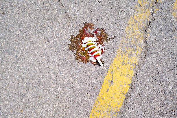 Colorful popsicle melting on hot asphalt on a summer day, creating a sticky mess next to a bright yellow painted line, epitomizing the heat of the season