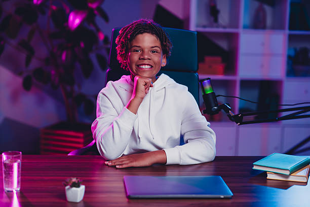 istock Young man with a microphone sitting indoors, engaging in online blogging or streaming, illuminated by colorful neon lighting 2236092013