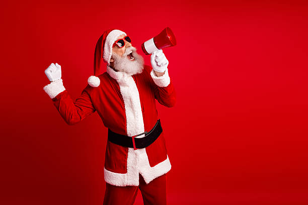 istock Energetic Santa Claus Shouting Cheerfully Into a Megaphone While Standing Against a Bright Red Background on Christmas 2236092249