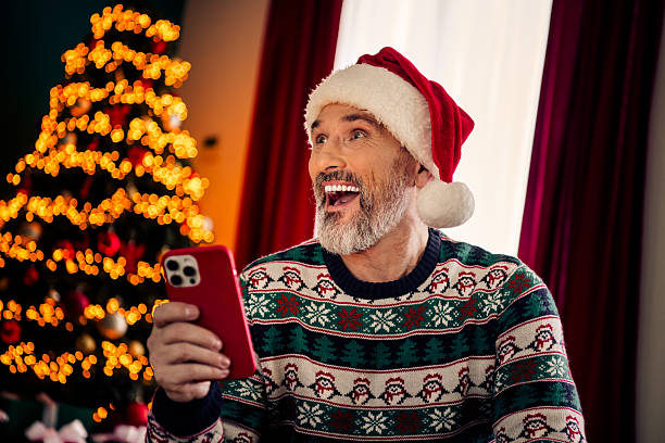 istock Excited elderly man holding a smartphone while celebrating Christmas at home with decorations and festive vibes 2236093190