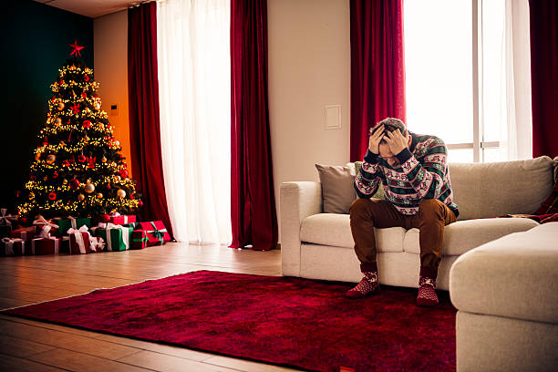 istock Man seated on a sofa in a festive room reflects during the holidays with a decorated Christmas tree nearby 2236093207