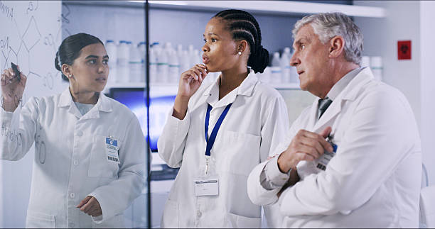istock People, scientist and writing on glass in lab for planning, equation and formula for experiment. Staff, notes and brainstorming for research, team investigation and medical information for vaccine 2236096376
