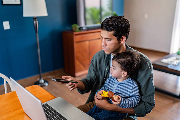 istock Young man working and using mobile phone while holding his baby son at home 2236096805