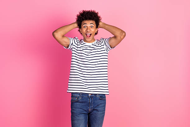 istock Cheerful young man with a striped shirt posing with joyful expression on a pink background, showcasing a fashion style 2236097298