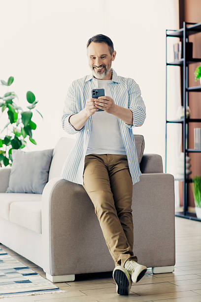 istock Mature businessman enjoying leisure time at home, using smartphone while dressed in casual professional attire, smiling confidently 2236098411