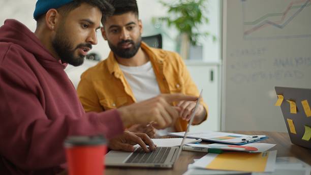 istock Small business startup founders informal corporate managers multiracial people talking diversity partners colleagues working in coworking office. Two Indian businessmen Hindu men discuss typing laptop 2236101295