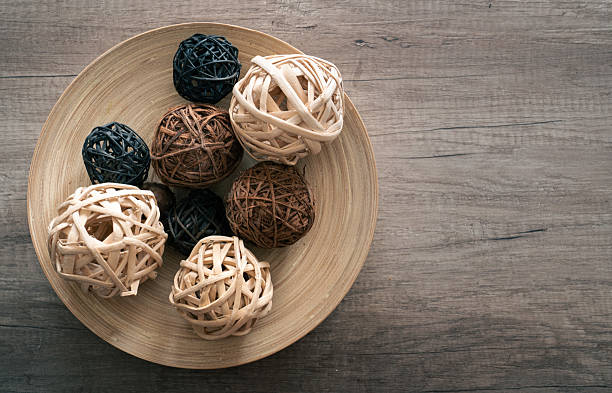 Top view of natural decorative wicker balls in a wooden bowl placed on rustic wooden table. Minimalistic home decor concept with copy space for text, suitable for interior design, lifestyle, or background use.