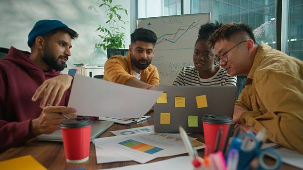 istock Focused concentrated informal casual startup business team considering paper document report information together talking solving finance problem multiethnic four people in office meeting with laptop 2236104524