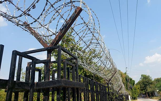 istock Low Angle View of Black Metal Security Fence Topped with Coiled Razor Wire 2236104526