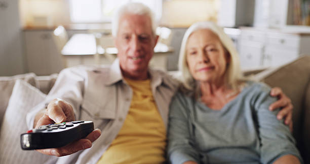 istock Senior couple, relax or watching TV with remote on sofa for online entertainment or channel in home. Elderly, man and woman with controller for movie subscription, bonding or retirement show in house 2236104708
