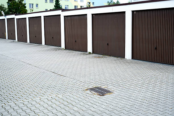 Garage units with brown metal doors and a storm drain on a paved yard. Symbol of urban infrastructure, storage and parking facilities.