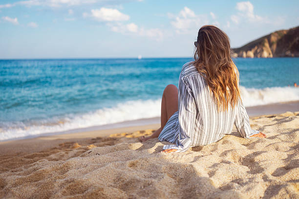 istock Relaxed Woman Sitting on Sandy Beach Overlooking Blue Ocean Waves 2236107542