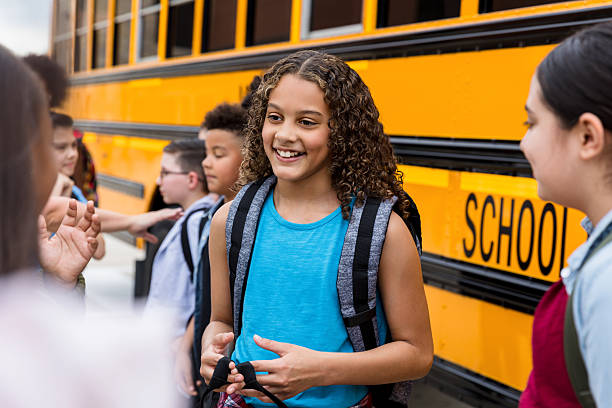 istock Happy elementary school girls chatting by school bus 2236109331