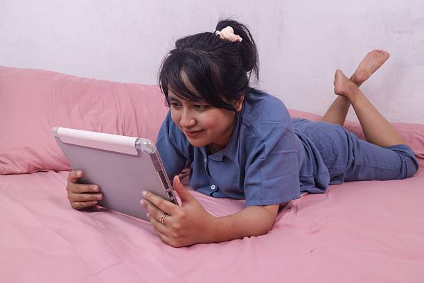 Beautiful asian woman wearing pajama lying on bed using tablet.
